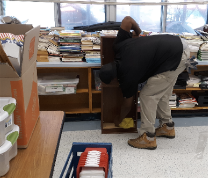 a Servpro worker cleaning a book case in a school 