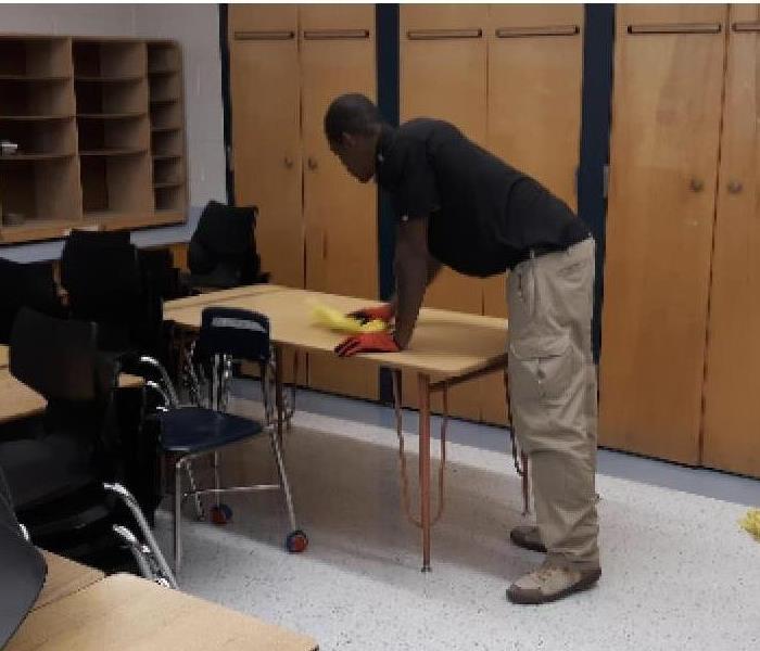 a Servpro worker cleaning a table in a classroom