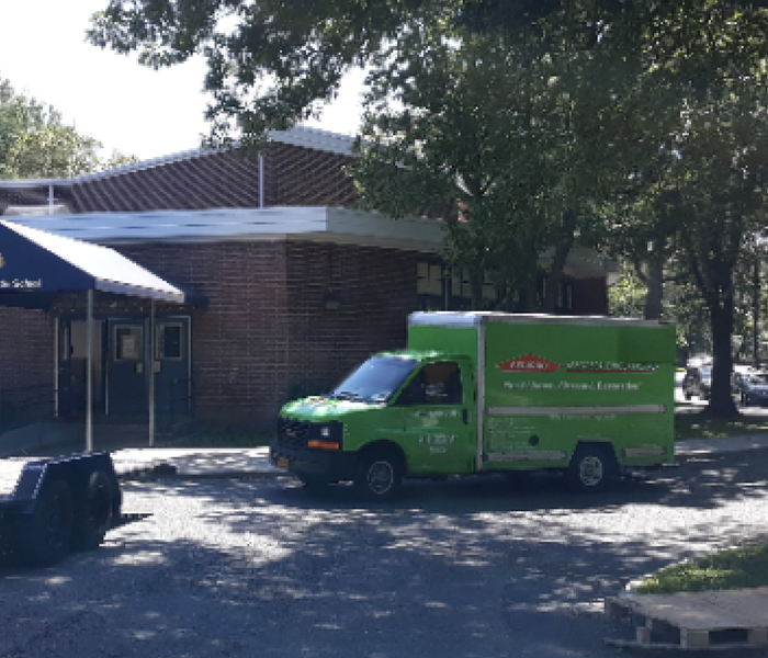 a green SERVPRO truck in front of the exterior of a school