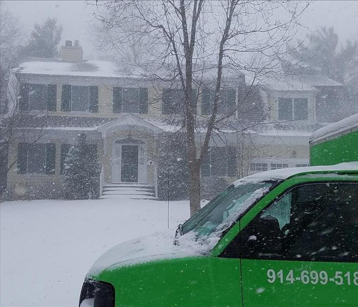 A SERVPRO truck sits in front of a large home during a snow fall. 