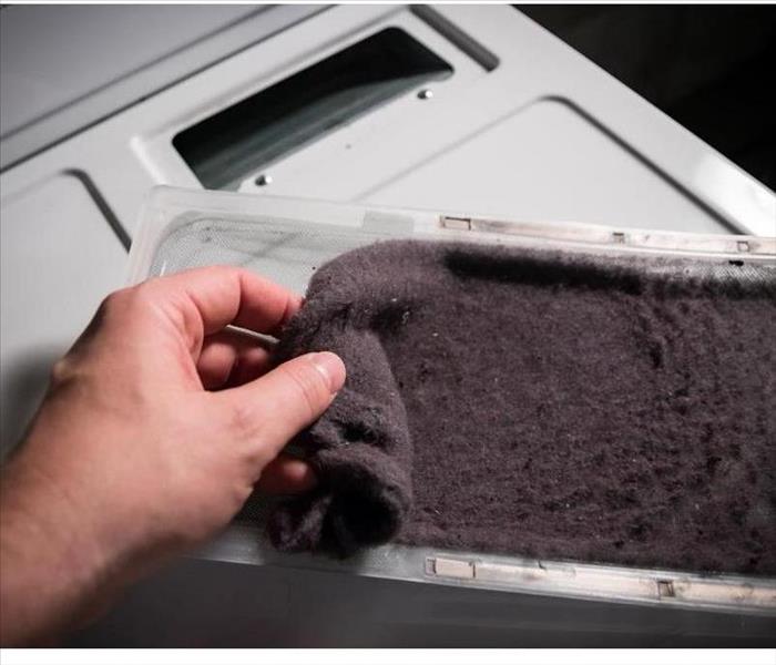 Hand cleaning accumulated clothing lint from trap in clothes dryer.